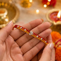 Marvel Silver Om Designer Rakhi featuring a silver-finish Om charm with crystal beads on a handcrafted red and yellow thread for Raksha Bandhan.