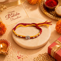 Marvel Silver Om Designer Rakhi with sparkling Om centerpiece, silver decorative beads, and red-yellow braided thread for Raksha Bandhan