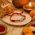 Marvel Silver Radha name rakhi for brother with yellow red braided thread and stone-studded silver-tone centre