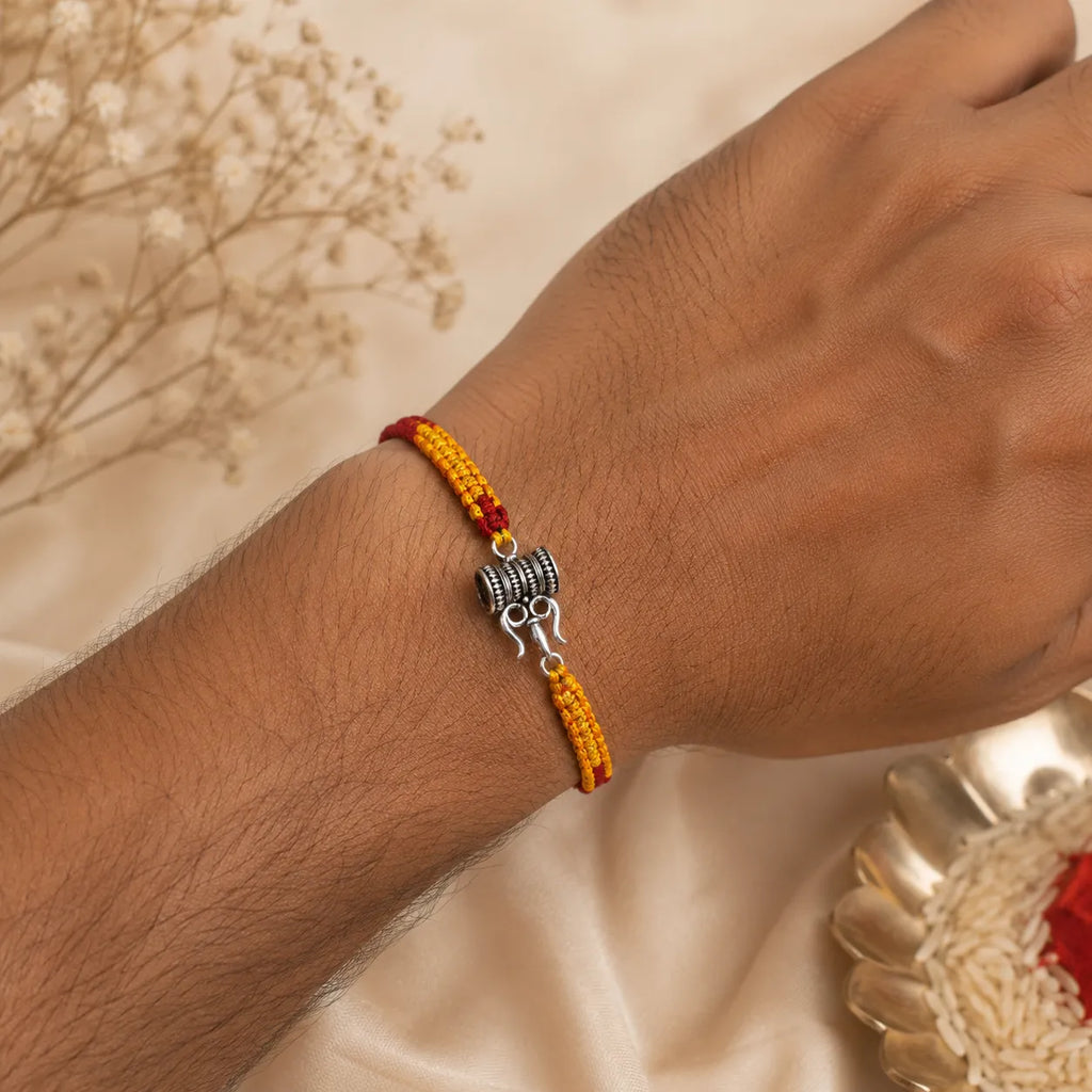 Marvel Silver Trishul Damru design rakhi with yellow red braided thread and silver-tone devotional charm