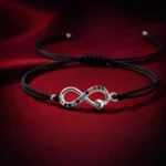 •A black cord bracelet featuring a silver infinity symbol accented with a tiny heart and colorful inlaid stones.