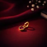 •A romantic heart-shaped pendant featuring a deep ruby-red gemstone set in a textured gold-toned border.