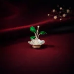 •A unique decorative silver ornament shaped like a small plant with vibrant green enamel leaves sitting in a silver base.